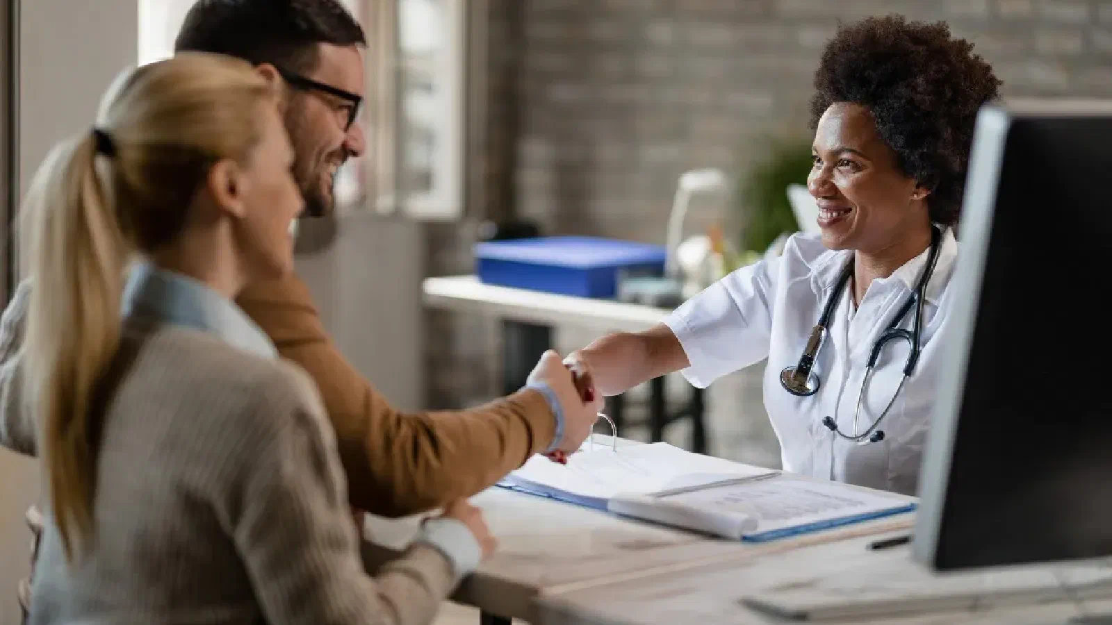 Médica cumprimentando um casal de pacientes no consultório